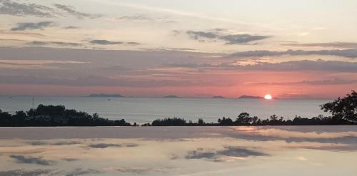 a sunset over the ocean with a reflection in a pool at Pearl Villa in Nathon