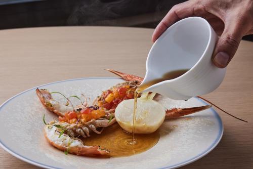 a person pouring sauce on a crab on a plate at UMITO Kamakura Koshigoe in Kamakura