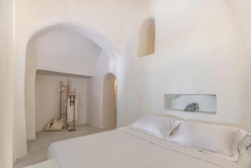 a white bedroom with a white bed and an archway at Pina Caldera Residence in Oia