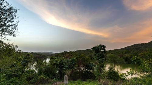 a rainbow in the sky over a river with trees at Dera Baghdarrah Nature Retreat Udaipur in Udaipur