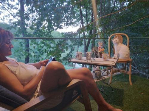 un homme assis sur une chaise à une table avec un chat dans l'établissement chalet sur pilotis en perigord, à Carsac-Aillac