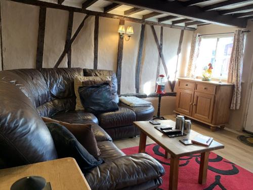 a living room with a leather couch and a table at Myrtle cottage in Dickleburgh