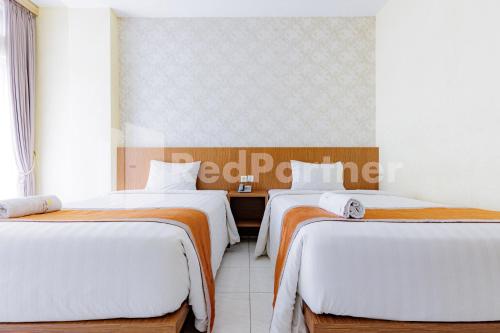 two beds in a room with white and orange sheets at De Malang Sweet Homestay Syariah Mitra RedDoorz in Malang