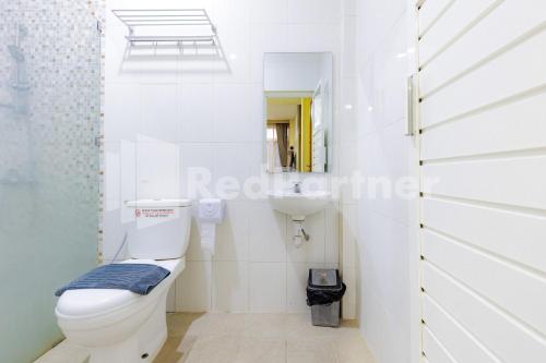 a white bathroom with a toilet and a sink at De Malang Sweet Homestay Syariah Mitra RedDoorz in Malang