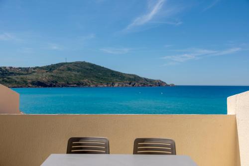 a table and two chairs on a beach with the ocean at Hôtel et Résidence Ta Kladia - Omigna in Cargèse