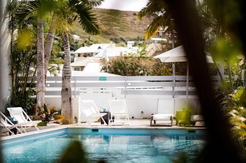 a swimming pool with white chairs and a white fence at Appartements Le Bleu des Roches Noires in Saint-Gilles les Bains
