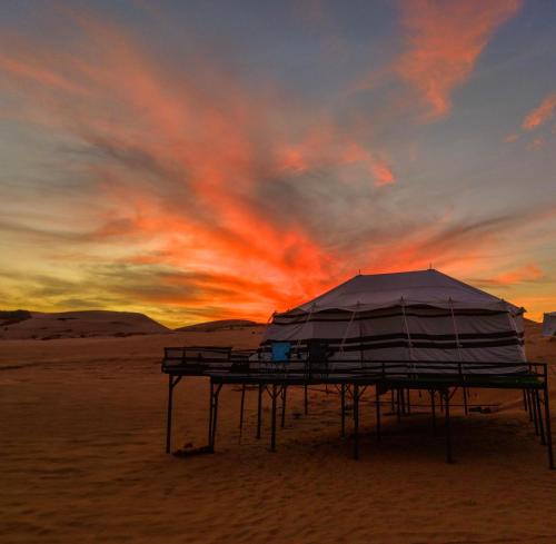 a tent on the beach with a sunset in the background at Mirage Desert Camp in Al Raka