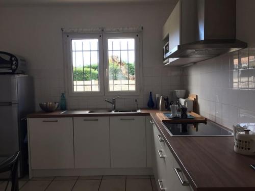 - une cuisine avec des placards blancs, un évier et 2 fenêtres dans l'établissement Bassin d'Arcachon Maison au calme, à Gujan-Mestras