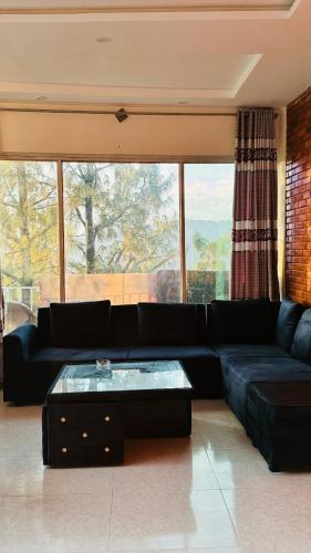 a living room with a black couch and a large window at Green view guest house nathiagali by room in Nathia Gali