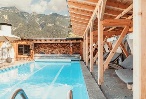 a pool with a wooden house with mountains in the background at Staudacherhof in Garmisch-Partenkirchen I Blick aufs Zugspitzmassiv I einzigartige Bayurvida Küche in Garmisch-Partenkirchen