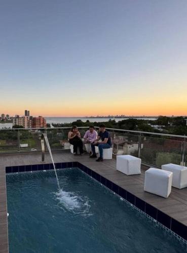 tre persone sedute su un tetto con piscina di Mono ambiente costanera a Encarnación