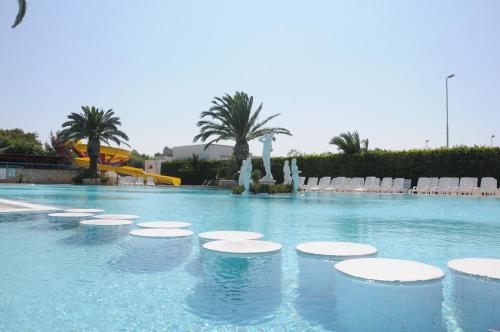 a large swimming pool with chairs and palm trees at Camping Villaggio Pineta Al Mare in Specchiolla 