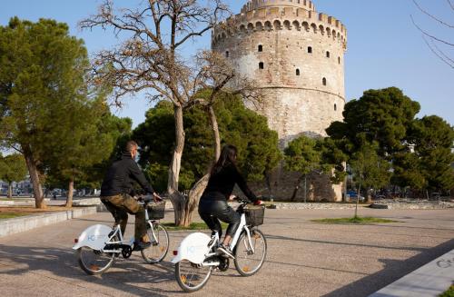 two people riding bikes in front of a white tower at Domotel Olympia in Thessaloniki