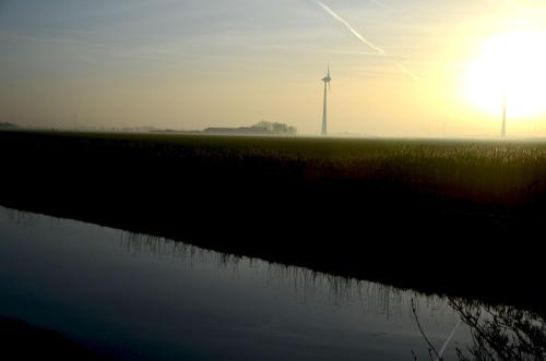a sunset with a windmill in the background and a body of water at Am Alten Hafen in Neuharlingersiel