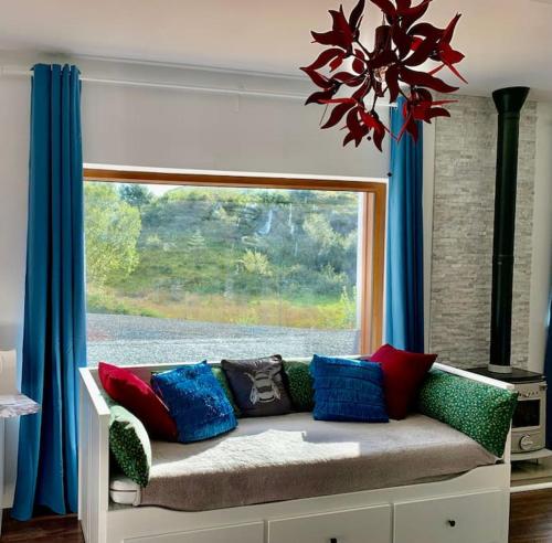 um sofá com almofadas coloridas sentado em frente a uma janela em Cosy Studio Cabin set in nature with stove em Killybegs