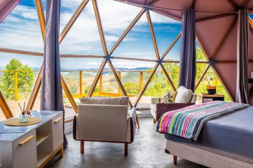 a room with a large window with a bed and chairs at Domo Geodésico para se conectar com as Nuvens in Paraibuna