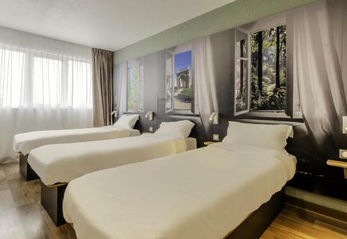 a row of beds in a hotel room with windows at B&B HOTEL Cambrai in Cambrai