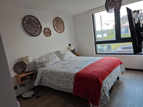 a bedroom with a bed with a red blanket and a window at Depa con piscina frente al Lago Llanquihue y vista al volcán in Puerto Varas