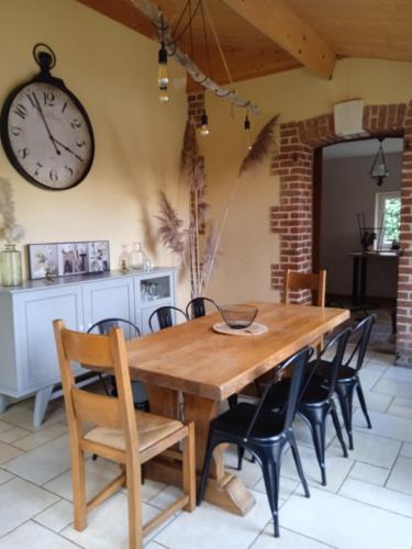 une table à manger avec des chaises et une horloge murale dans l'établissement Gite meublé avec étang en lisière de forêt., à Les Grandes Prouillères