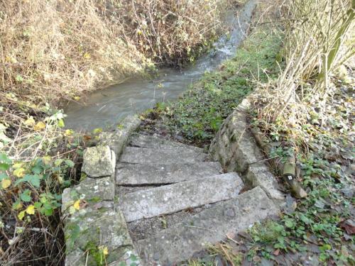 a set of stone steps leading to a stream at Au Petit Ry in Treignes