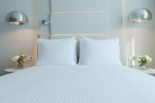 a white bed with two pillows and flowers on two tables at NH Monterrey La Fe in Monterrey