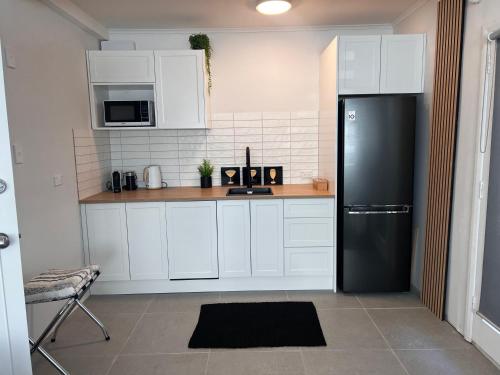 Una cocina con gabinetes blancos y un refrigerador negro. en Studio by the bays, en Auckland