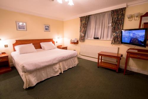 a hotel room with a bed and a flat screen tv at Harefield Manor Hotel in Romford