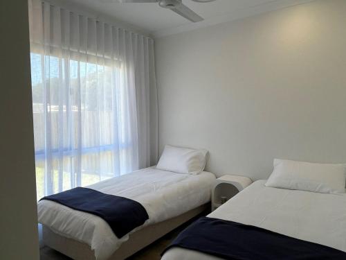 two beds in a small room with a window at 6 Yeri Drive - Rainbow Shores. Aircon. Pets Welcome. Walk to beach in Rainbow Beach