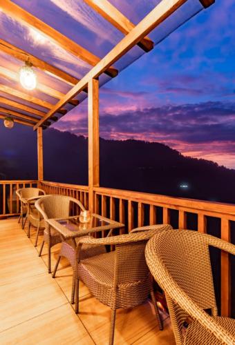 a deck with chairs and tables and a sunset at The Devan Wood Resort in Dhanaulti