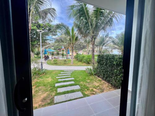 a view from a door of a walkway with palm trees at The Vista Beach Resort Phan Thiết in Phan Thiet