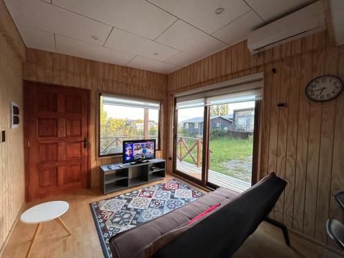a living room with a couch and a tv and windows at Cabaña Los Maquis en Castro in Castro