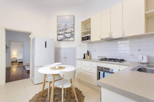 a kitchen with white cabinets and a white table at The Coastal Nest - South Fremantle in South Fremantle