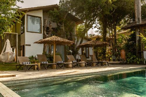 a pool with chairs and umbrellas next to a house at Hotel Boutique Bahia Bonita in Trancoso