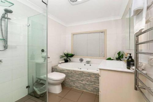 a bathroom with a tub and a toilet and a shower at Tranquility with Spa & Jetty in Woy Woy