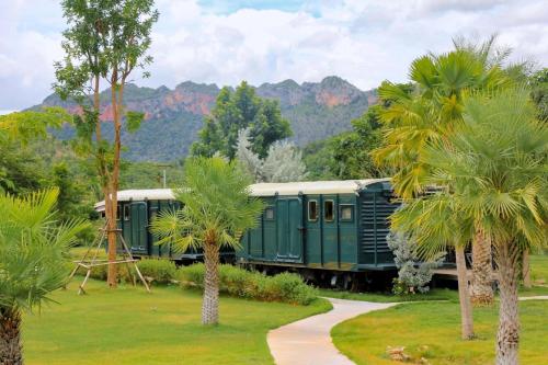 a green train with palm trees and mountains in the background at Nex Station Kanchanaburi in Kanchanaburi