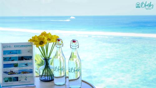two bottles on a table with flowers and a book at Blue Sky Beach in Hulhumale