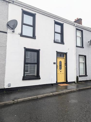 a white building with a yellow door and windows at Ivy Townhouse Derry in Derry Londonderry