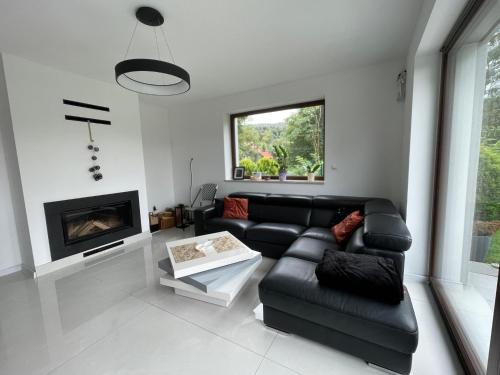 a living room with a black leather couch and a fireplace at Pustelnika Chatka nad Brennicą in Brenna