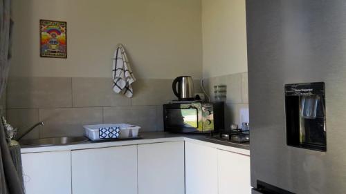 a kitchen with white cabinets and a microwave and a refrigerator at Kombi Cove Bloubergstrand in Cape Town