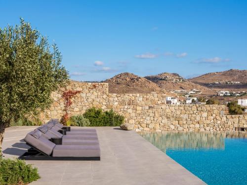 a row of benches next to a stone wall and a pool at Blue Eye Grand Villa Mykonos in Kalafatis