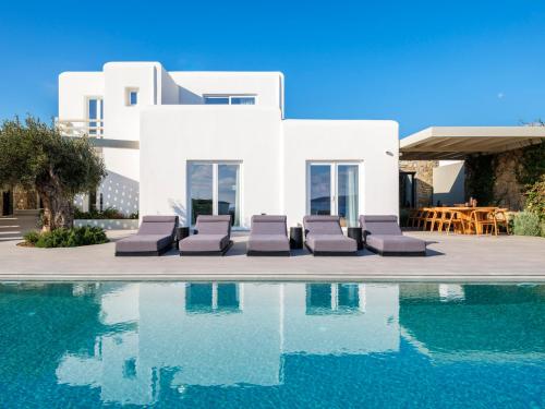 a swimming pool with lounge chairs and a house at Blue Eye Grand Villa Mykonos in Kalafatis