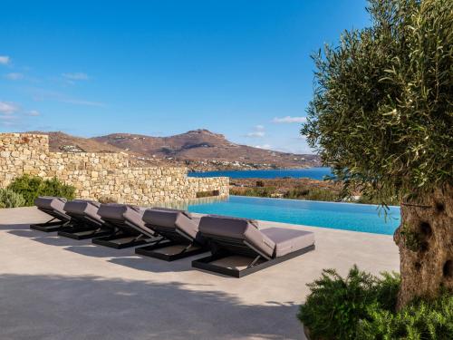 a row of lounge chairs next to a swimming pool at Blue Eye Grand Villa Mykonos in Kalafatis