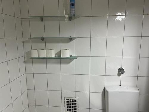 a white tiled bathroom with a toilet and a shelf at Monteurwohnung in Marl - Schiller - 1OGL in Marl
