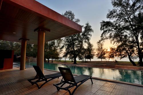 a couple of chairs sitting next to a swimming pool at Coriacea Beachfront Boutique Phuket Resort - SHA Plus in Mai Khao Beach