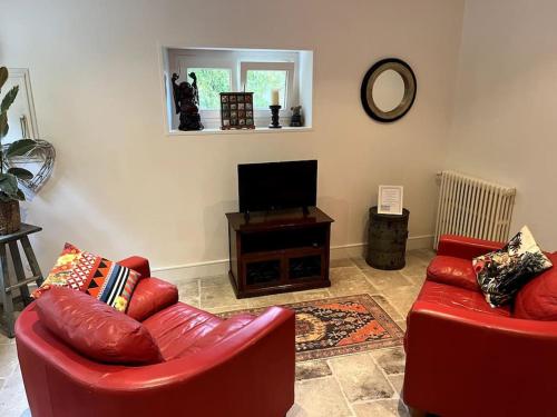 a living room with two red chairs and a flat screen tv at The Coach House in Saint-Côme-de-Fresné