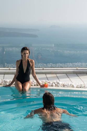 a woman sitting in a swimming pool next to a man at Santorini Princess Spa Hotel in Imerovigli