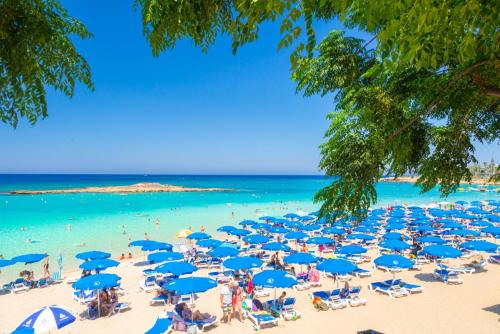 a beach with blue umbrellas and people in the water at Villa Koula in Paralimni