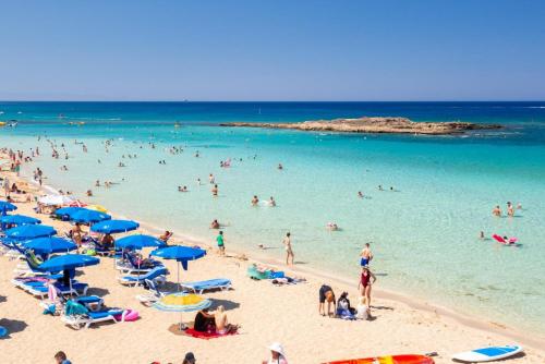 a crowd of people on a beach with blue umbrellas at Villa Koula in Paralimni