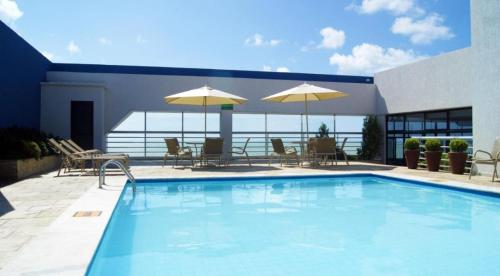 a swimming pool with tables and chairs and umbrellas at HOTEL TAMBAÚ FLAT EXCLUSIVE apt particular in João Pessoa
