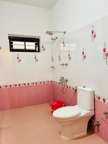 a pink bathroom with a toilet and a red bucket at Marari Beach Homestay in Mararikulam